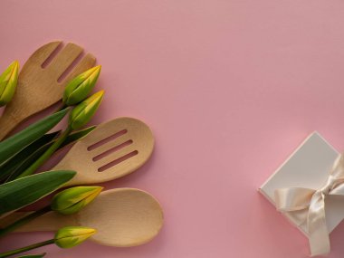 Sarı yeşil lale çiçekleri mutfak aletleri ve pembe arka planda beyaz hediye kutusu ve fotokopi alanı. Kadınlar ve Anneler Günü tebrik kartı. Doğum günü notu. Utensil buket düz yatıyordu.