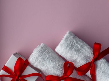 İki beyaz havlu ve beyaz kağıda sarılı hediye kutusuyla yatıyordu. Kırmızı kurdeleli pembe kağıt kaplama havlular. Sevgililer günü spası, banyo, kişisel bakım ve vücut bakımı konsepti. Boşluğu kopyala.