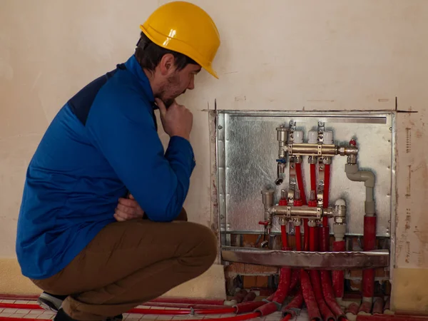 Underfloor heating installation. Water floor heating system interior. Plumbing pipes in apartment during renovation. Underfloor heating manifold. The employee think about the problem in heating system