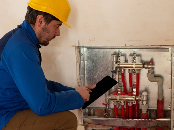 Underfloor heating installation. Water floor heating system interior. Plumbing pipes in apartment during renovation. Underfloor heating manifold. An employee adjusts the heating system via a tablet.