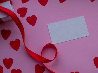 Bir sürü kalp şeklinde kâğıt, beyaz hediye kutusu ve mesaj için yeri olan düz bir yerde yatıyordu. Kırmızı kalp kağıdı arka planında hediye kutusu var. Tebrik kartı, hediye. Sevgililer Günü tatili konsepti. 14 Şubat.