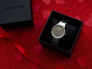MVMT brand. Gift box with silver watch is on red heart paper background, top view. Greeting card, present. Valentines day holiday concept. Flat lay with an elegant wristwatch. February 14th.