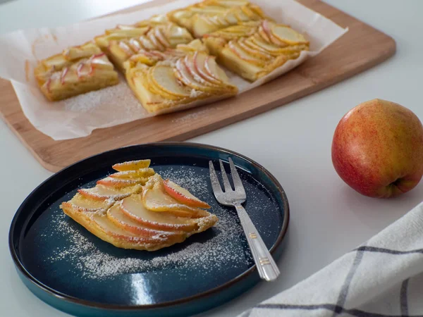 stock image Apple vanilla squares. Homemade apple pie topped with slices of apples. Serving of delicious fruit vanilla cake on a dark plate with fork. Thin slices of apples are stuffed tightly and powdered sugar.