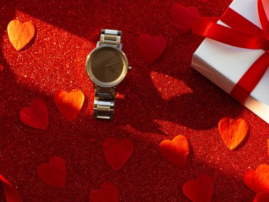 Hediye kutusu ve gümüş saat kırmızı kalp kağıdının arka planında, üst tarafta. Tebrik kartı, hediye. Sevgililer Günü tatili konsepti. Düz bir kol saati ve metin için boşluk ile yatıyordu.