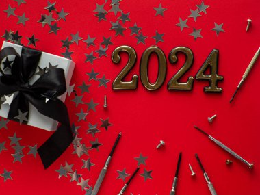 2024 ve inşaat aletleri ve kırmızı arka planda paketlenmiş hediye. Noel ya da yeni yıl için tebrik kartı. Evi onar. Erkek için hediyeler. Erkeklere hediye almak..