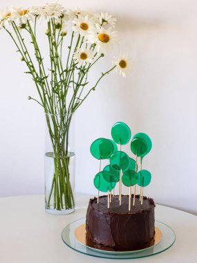 Beyaz arka planda yeşil şekerli çikolatalı pasta ve fotokopi alanı. Kahverengi kremalı doğum günü pastası. Cam tezgahta kahverengi kek, beyaz masada papatya ve şeker..