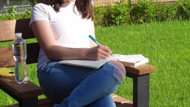 ベンチに座り 公園で本を読んでいるブルネットの女性 教育学校と人々のコンセプト キャンパスでベンチで勉強する女性学生 本を持って座っている少女 水と執筆のボトル — ストック動画