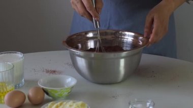 Bir kadın kek için gevşek malzemeleri yoğurur ya da çırpıcıyla metal bir kaseye kek hamuru koyar. Doğum günü pastaları için hamur hazırlığı. Kek, turta ve kek yapmak için bir adım. Pişirme süreci.