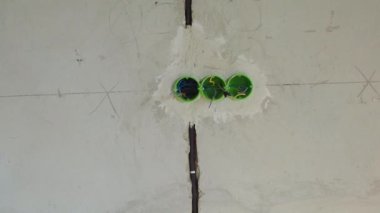 Duvardaki delinmiş deliklere yerleştirilen prizler ya da anahtarlar için yeşil yuvarlak plastik arka kutu. Yeni elektrik tesisatı, duvarda delik, yenileme konsepti. Elektrik kablosu kurulumu.