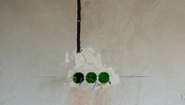 Duvardaki delinmiş deliklere yerleştirilen prizler ya da anahtarlar için yeşil yuvarlak plastik arka kutu. Yeni elektrik tesisatı, duvarda delik, yenileme konsepti. Elektrik kablosu kurulumu.