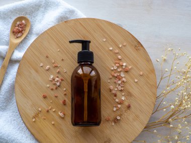 Doğal cilt bakımı SPA güzellik ürünü tasarımı. Kehribar cam şişe ahşap tabakta deniz tuzu ile. Bej arka planda mineral organik yağ kozmetiği. Model Yukarı. Yüz ve vücut tedavisi. Düz yatıyordu.