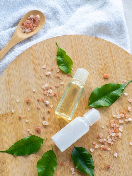 Composition with green leaves, beauty products bottles and sea salt in wooden spoon. Wellness card. Body and skincare concept with copy space. Hygiene and spa, relaxation as a gift for holidays.