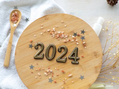 2024 ve kış cilt bakımı SPA güzellik ürünleri tasarımı. Deniz tuzu, yıldız ve koni içeren ahşap tabağın yanındaki beyaz şişe. Bej arka planda mineral organik yağ kozmetiği. Noel hediyesi konsepti. Düz yatıyordu