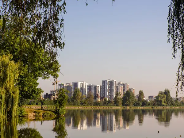 Yazın mavi gökyüzüne karşı parkta bir yerleşim yeri. Yeni modern apartman binaları çevresi yeşil ağaçlarla çevrili. Modern iş gökdelenleri, yaşam alanları.