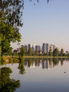 Yazın mavi gökyüzüne karşı parkta bir yerleşim yeri. Yeni modern apartman binaları çevresi yeşil ağaçlarla çevrili. Modern iş gökdelenleri, yaşam alanları.