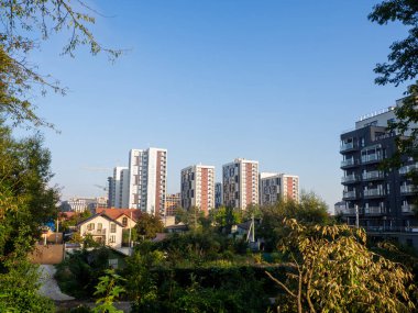 Yazın mavi gökyüzüne karşı parkta bir yerleşim yeri. Yeni modern apartman binaları çevresi yeşil ağaçlarla çevrili. Modern iş gökdelenleri, yaşam alanları.