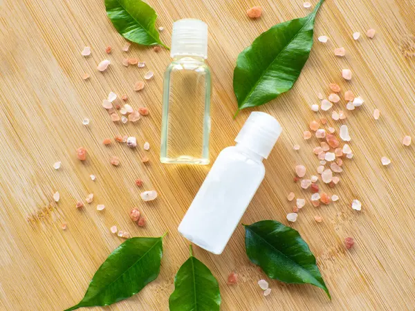Composition with green leaves, beauty products bottles and sea salt on wooden background. Wellness card. Body and skincare concept with copy space. Hygiene and spa, relaxation as a gift for holidays.