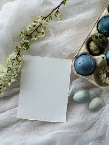Blue painted easter eggs. Dyed Easter eggs with marble stone effect light blue color on white tablecloth background with cherry blossom. Eggs background with copy space, Ester holiday postcard concept
