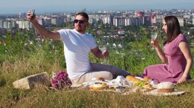 Güneş gözlüklü şık bir adam ve uzun pembe elbiseli bir kadın battaniyeye oturup telefonda selfie çekiyorlar. Genç çift yaz meyveleri, hamur işleri ve içeceklerle piknik yapıyor. Randevu. Boşluğu kopyala