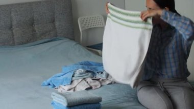 Yatak odasında temiz havlu katlayan bir kadın. Evde çamaşırları düzenlemek. Yıkandıktan sonra havlu. Minimalizm yaşam tarzı ve Japon katlama sistemi kavramı. Dolabı toparla.