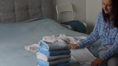 Yatak odasında temiz havlu katlayan bir kadın. Evde çamaşırları düzenlemek. Yıkandıktan sonra havlu. Minimalizm yaşam tarzı ve Japon katlama sistemi kavramı. Dolabı toparla.