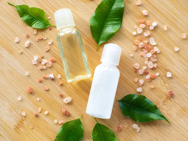 Composition with green leaves, beauty products bottles and sea salt on wooden background. Wellness card. Body and skincare concept with copy space. Hygiene and spa, relaxation as a gift for holidays.