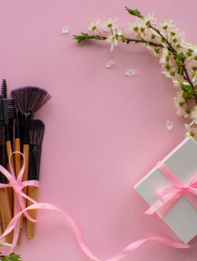 Bir buket kozmetik fırça, pembe bir kurdeleyle bağlanmış, arka planda pembe bir fiyonk, kiraz çiçekleri ve fotokopi alanı. Kadınlar ve Anneler Günü hediyesi. Güzellik ve kadınlık kavramı. İnternetten hediye almak.