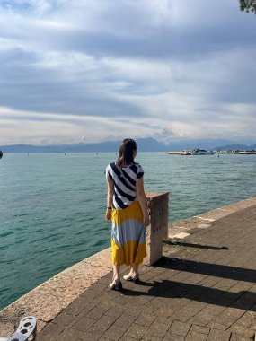 Veneto, Verona 'daki lago di Garda' nın su manzarasının tadını çıkaran uzun elbiseli kadın. İtalya 'nın en büyük kıyısı Garda Gölü. Peschiera del Garda 'dan görünen Garda Gölü' nün muhteşem manzarası.