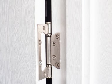 Bu resim, kapı pervazına takılmış yıpranmış çelik kapı menteşesinin yakın çekimini gösteriyor. Detaylar, ev onarımı veya yenileme temaları için ideal yorgunluk ve giysiyi vurguluyor.