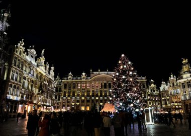 Brüksel, Belçika 'da tarihi binalar ve hareketli bir Noel pazarı ile çevrili ışıltılı ışıklar ve süslemelerle süslenmiş Grand Place gece görüşü.
