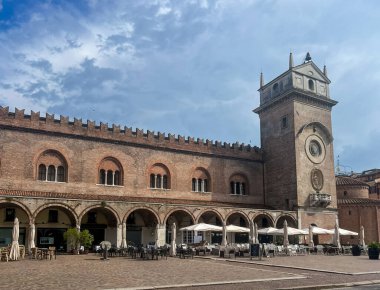 Mantova şehir meydanında muhteşem Palazzo della Ragione saat kulesiyle, Piazza delle Erbe 'de tarihi mimarisi ve kilisesi ile şık kemer yolları altında açık hava restoranlarıyla sergileniyor.