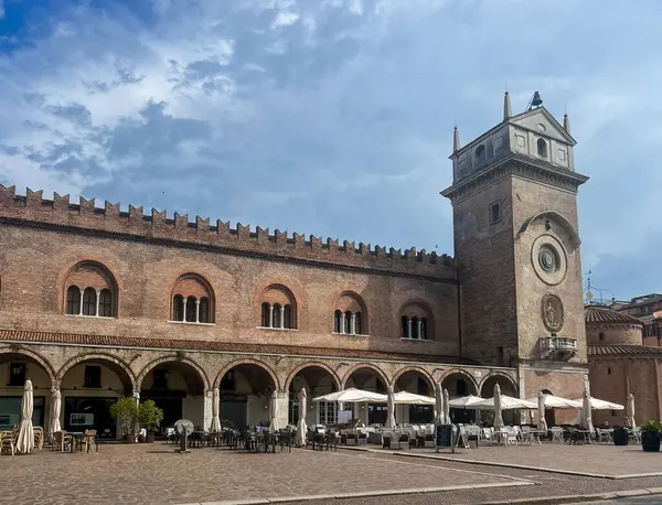Mantova şehir meydanında muhteşem Palazzo della Ragione saat kulesiyle, Piazza delle Erbe 'de tarihi mimarisi ve kilisesi ile şık kemer yolları altında açık hava restoranlarıyla sergileniyor.