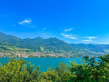 İtalya 'daki mavi gökyüzünü yansıtan sakin bir Iseo gölünün olduğu çarpıcı bir manzara. Yeşillik tarafından çerçevelenmiş görkemli dağlar uzaklardan yükselir. Huzurlu ve görkemli bir manzara yaratır..