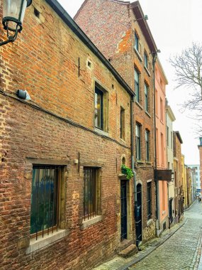Bu görüntü Brüksel, Belçika 'daki tarihi tuğla bir binanın büyüleyici dış görünüşünü yansıtıyor. Fotoğrafta arka planda çeşitli binalarla sıralanmış bir kaldırım taşı caddesi sergileniyor..