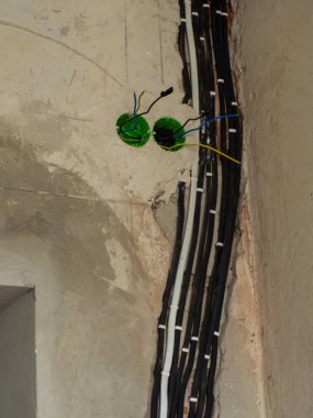 Bu görüntü, yenileme çalışmaları sırasında bir duvar içinde elektrik kablolarının kurulumunu yakalar. Odak noktası siyah kablolar. Elektrik tesisatının karmaşık detaylarını vurguluyorlar..