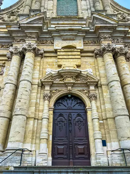 Bu görüntü, Leuven 'deki barok bir kilisenin çarpıcı bir ön görüntüsünü yakalıyor. Karmaşık taş cephesini, ön kapıya uzanan görkemli merdivenlerini ve parlak mavi gökyüzünü gösteriyor..