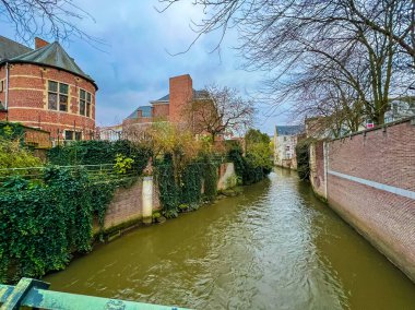 Leuven 'deki pitoresk kanal, çarpıcı bulutlu bir gökyüzünün altında yemyeşil çitler ve canlı kırmızı tuğlalarla çevrilidir. Doğa ve mimarinin mükemmel bir karışımı. Belçika