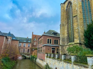 Leuven 'deki tarihi kasaba evleriyle yan yana duran ve berrak mavi gökyüzünün altında akan sakin bir kanalla tamamlanan gotik bir kilisenin manzarası, şehirlerin zengin mimari mirasını gözler önüne seriyor..