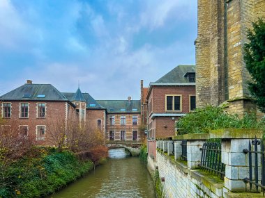 Leuven 'deki tarihi kasaba evleriyle yan yana duran ve berrak mavi gökyüzünün altında akan sakin bir kanalla tamamlanan gotik bir kilisenin manzarası, şehirlerin zengin mimari mirasını gözler önüne seriyor..
