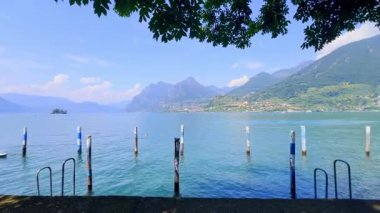 İtalya 'daki mavi gökyüzünü yansıtan sakin bir Iseo gölünün olduğu çarpıcı bir manzara. Yeşillik tarafından çerçevelenmiş görkemli dağlar uzaklardan yükselir. Huzurlu ve görkemli bir manzara yaratır..