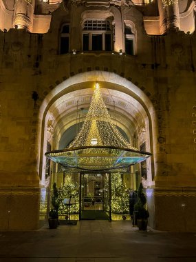 Budapeşte 'de büyük pencereleri ve dekoratif mimarisi olan avizeleri olan bir binaya giriş. Bina, kapılarının üzerindeki kemerlerden sarkan ışıklarla Noel için dekore edildi. Gece vakti.