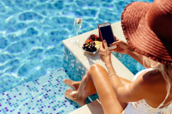 女性は屋外のスイミングプールでリラックスします 水着の美しい女性モデルはシャンパンを飲み 果物を食べる 高級リゾートでの夏休み時間 ロイヤリティフリーのストック写真
