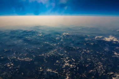 View from the airplane window at the setting sun and mountains crossed by clouds