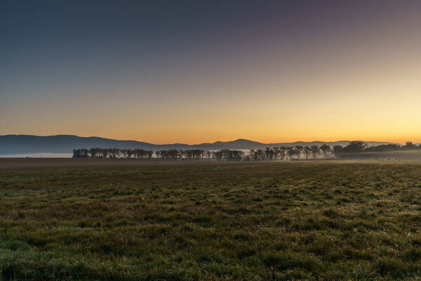 Beautiful sunrise over the mountains in the area of still shaded farmland