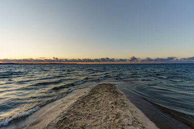 Günbatımı, dalgalı deniz ve kum manzaralı Rewal burnu bölgesinde.