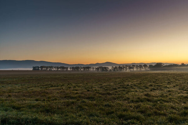 Beautiful sunrise over the mountains in the area of still shaded farmland