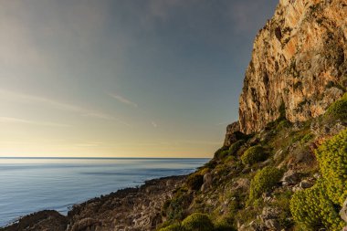 Kayalık dağ zirvelerinin ve duvarların indiği ılık denizin üzerinde güzel bir günbatımı..