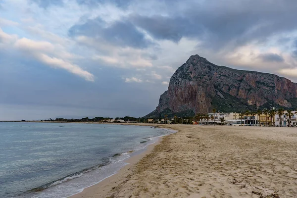 Güneşin batışında arka planında kayalık bir dağ olan güzel bir Sicilya plajı manzarası.