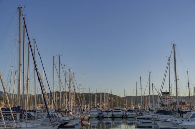 Sakin bir limanda yelkenli ve yatları olan bir liman, güneşle güzelce aydınlatılmış.