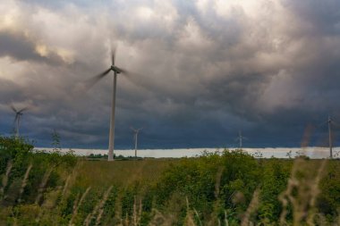 Yenilenebilir enerji kaynaklarından elektrik üreten yel değirmenlerinin manzarası çayır ve bulutların arka planına karşı.